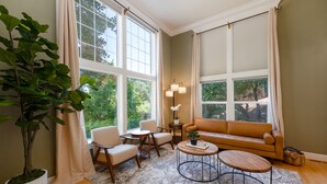 A living room with a sofa, chairs, a coffee table, and a large window with curtains.