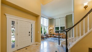 A spacious hallway with a double door, a staircase with a handrail, and a seating area with a sofa and chairs.