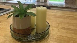 A kitchen with white cabinets, a window with a view of greenery, and a glass tray with a potted plant and candles.