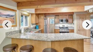 Une cuisine dotée de plans de travail en granit, de meubles en bois et d’un îlot central avec des tabourets de bar.