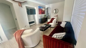 En moderne stue med en hvid lænestol, en rød sofa, et sort sofabord og en hvid pejs.
