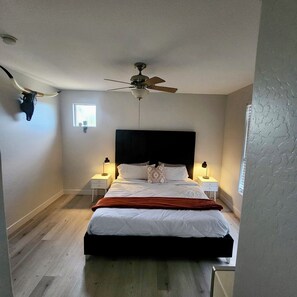 Ein Schlafzimmer mit einem Bett, Deckenventilator, zwei Nachttischlampen, einem Fenster und einem Wandbild eines Stierschädels.