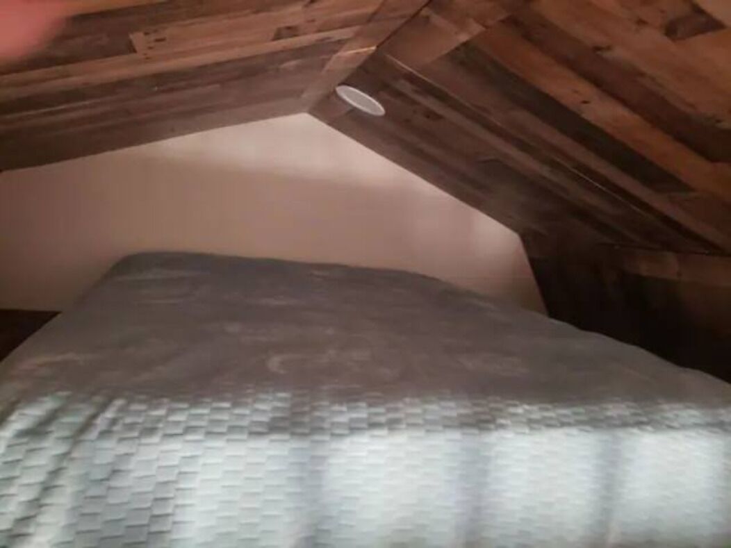 A room with a sloped ceiling, a bed with a patterned bedspread, and a visible ceiling vent.