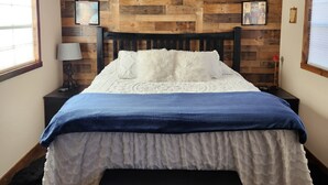 Une chambre à coucher avec une tête de lit en bois, un lit recouvert d’une literie blanche et bleue, deux tables de chevet avec des lampes et des tableaux encadrés accrochés au mur.