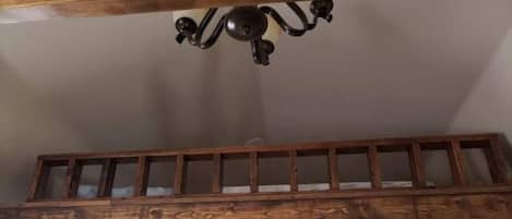 Una habitación tipo loft con vigas de madera a la vista, una escalera de madera, un ventilador de techo y un adorno en forma de estrella.