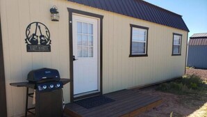 Un petit bâtiment d’un seul étage, doté d’une porte et de fenêtres, d’un barbecue à l’extérieur et d’une terrasse en bois.