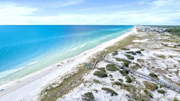 A coastal beach with a wooden walkway, sandy shore, and clear blue waters.