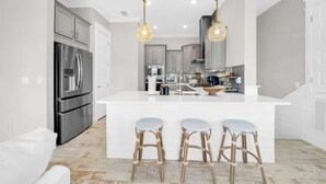 A modern kitchen with a central island, stainless steel appliances, and hanging pendant lights.