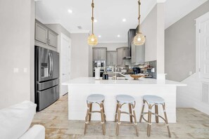 A modern kitchen with a central island, stainless steel appliances, and hanging pendant lights.