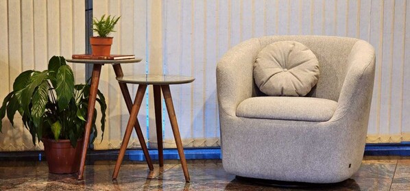 A room with a grey armchair, a small round table with a potted plant, and a large potted plant.