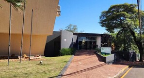 A hotel entrance with a paved pathway leading to the entrance, a signboard, and a building with a modern design.