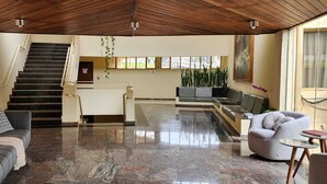 Amplia sala de estar con techo de madera oscura, una escalera, una zona de cocina con televisor y un rincón de estar con sofá y sillón.