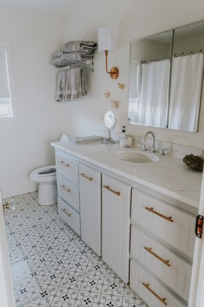 A bathroom with a white vanity, a large mirror, a sink, and a toilet. - MoonShiner Farm - Shiner TX (Shiner)