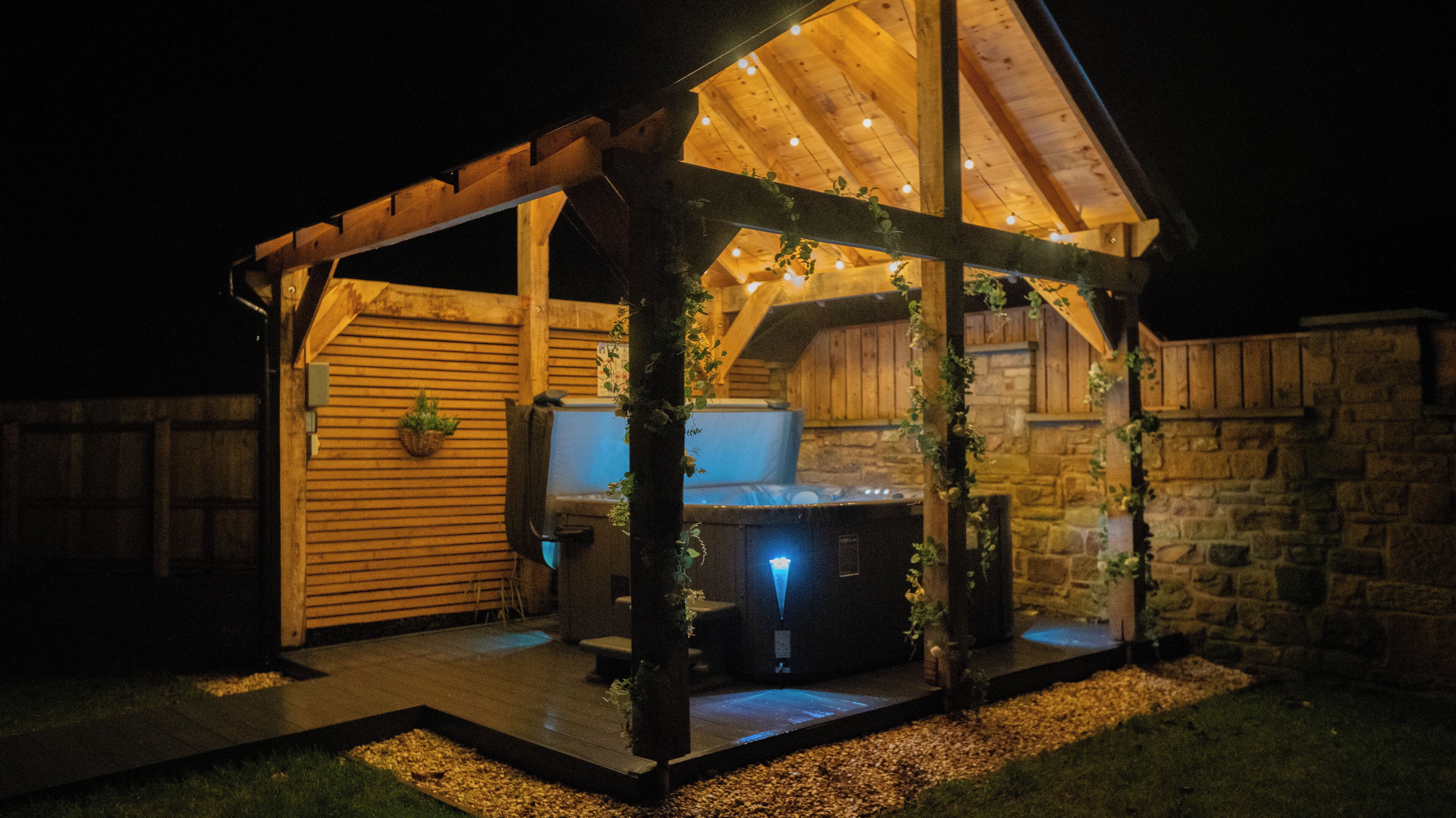 Ein hölzerner Pavillon mit Whirlpool, umgeben von Steinmauern und einem Holzzaun.