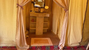 A room with a bed, a mirror, a sink, and a shelf. - Arena Desert Camp & Activitys (Merzouga)