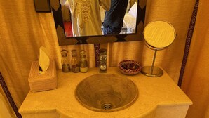A bathroom with a stone sink, a mirror, a tissue box, and a small basket. - Arena Desert Camp & Activitys (Merzouga)