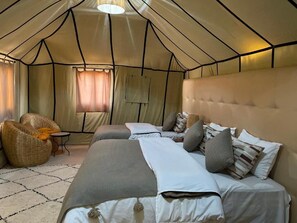 A tent-style room with two beds, a small table, and a wicker chair. - Arena Desert Camp & Activitys (Merzouga)