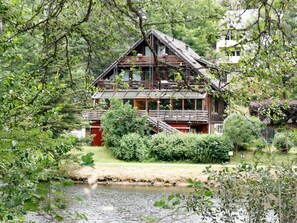 Une cabane rustique avec une façade en bois, un balcon et un étang au premier plan.
