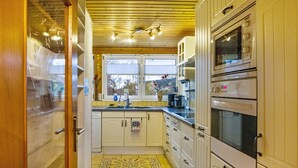 A kitchen with wooden cabinets, a sink, a stove, and a window with a view of trees. - Holiday flat "am Talsee", with lake view, balcony and Wifi (Unterkirnach)