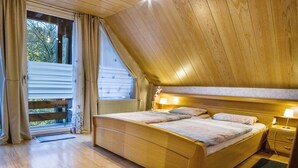 A bedroom with a sloped ceiling, a bed with two pillows, a nightstand with a lamp, and a window with curtains. - Holiday flat "am Talsee", with lake view, balcony and Wifi (Unterkirnach)