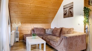 Ein gemütliches Zimmer mit Holzboden, einem braunen Sofa, einem weißen Tisch und einer kleinen Pflanze.