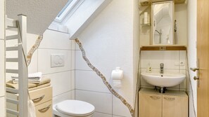 Un baño con inodoro, lavamanos, toallero y zona de ducha.