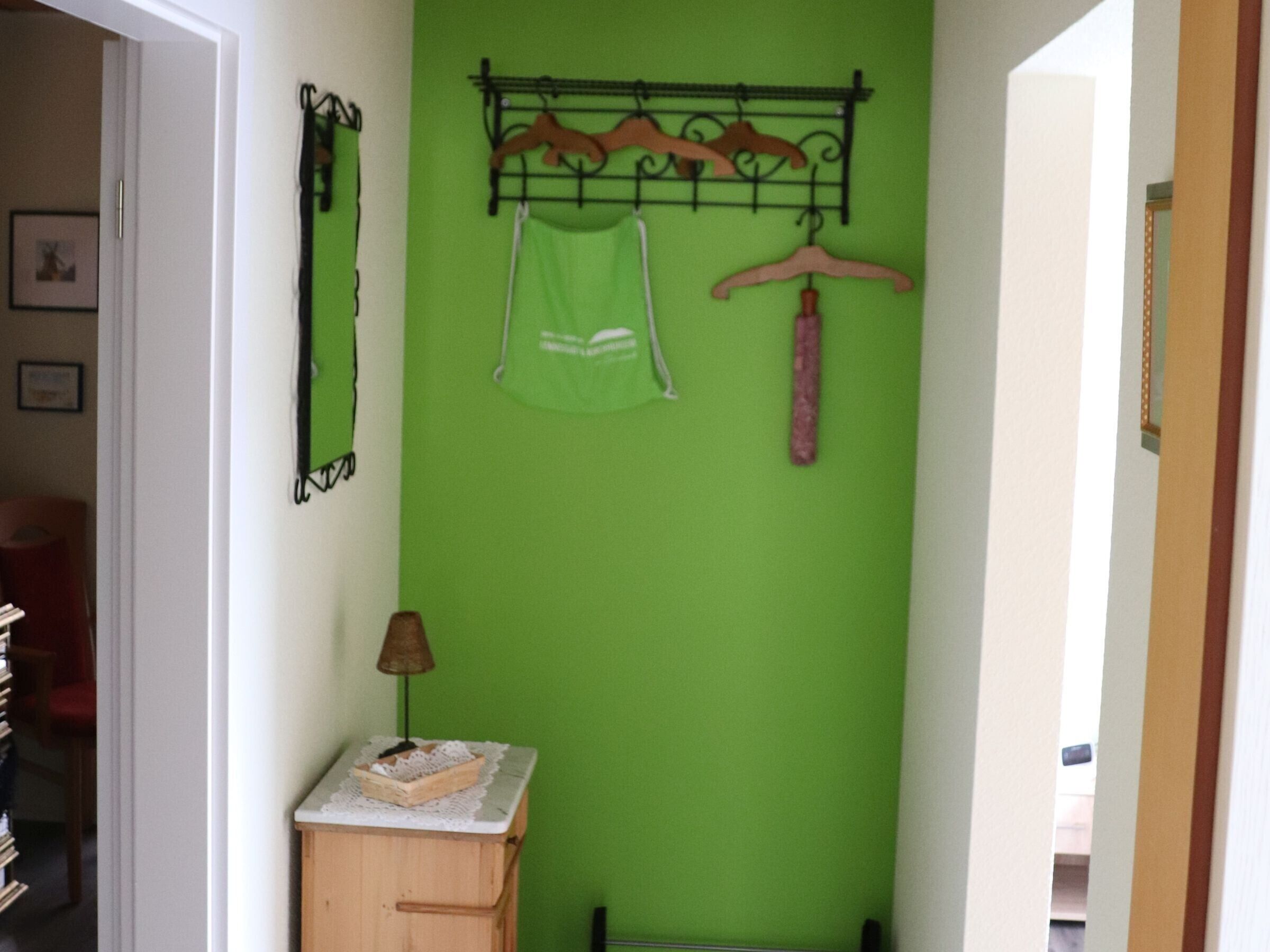 Ein Zimmer mit grüner Wand, einem Holzschrank mit Spitzendesign, einem hängenden Metallregal mit Kleidung und einer Tür zu einem anderen Raum.