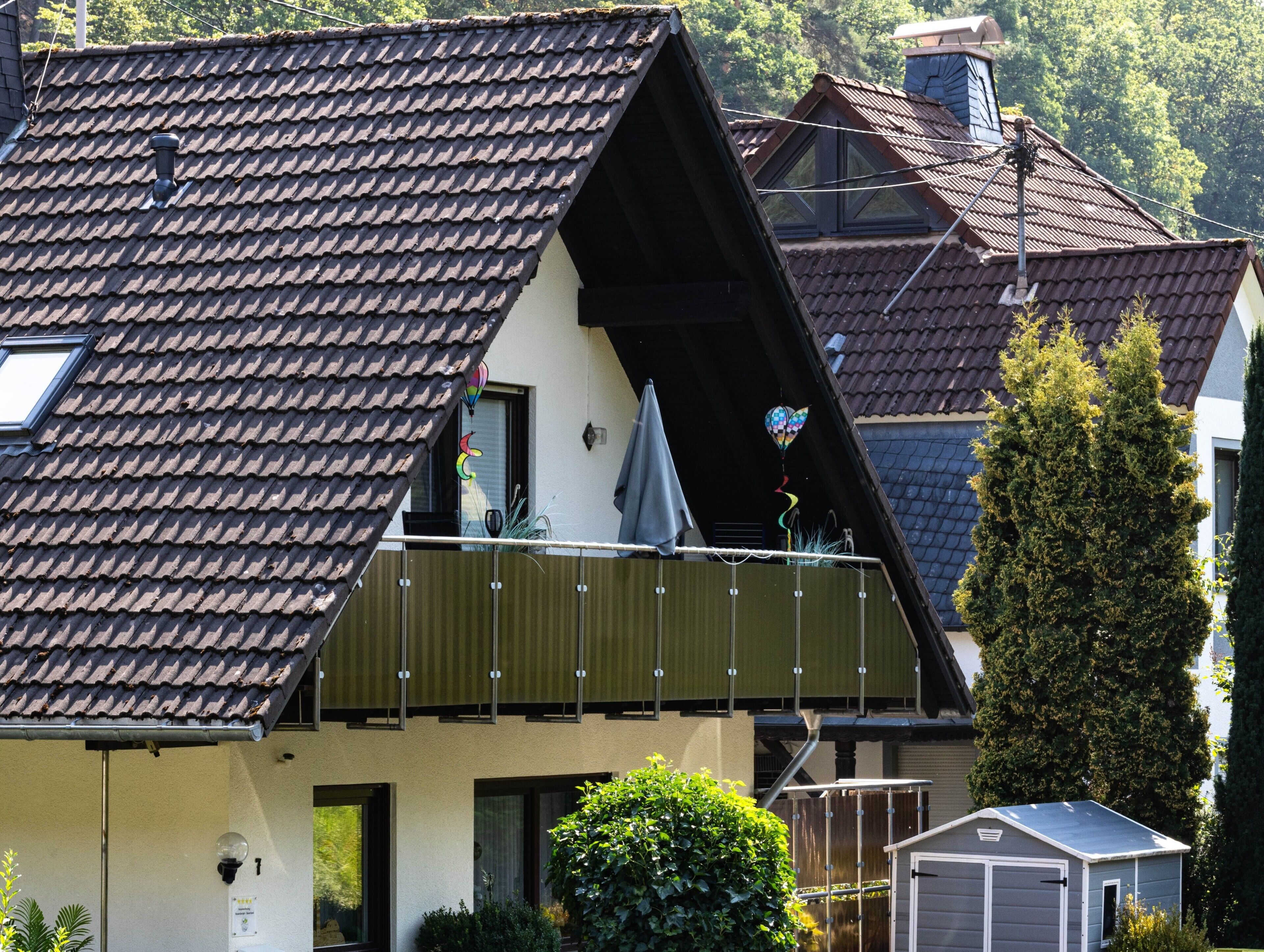 A residential building with a sloped roof, a balcony with a railing, and a small shed in the foreground.