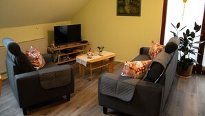 Un salon avec deux canapés, une table basse, un téléviseur et une plante.