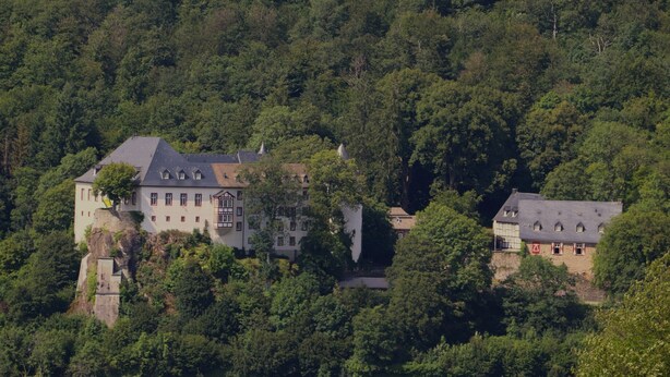 Un grand bâtiment à étages, doté d’un toit en pente et entouré d’une forêt dense.