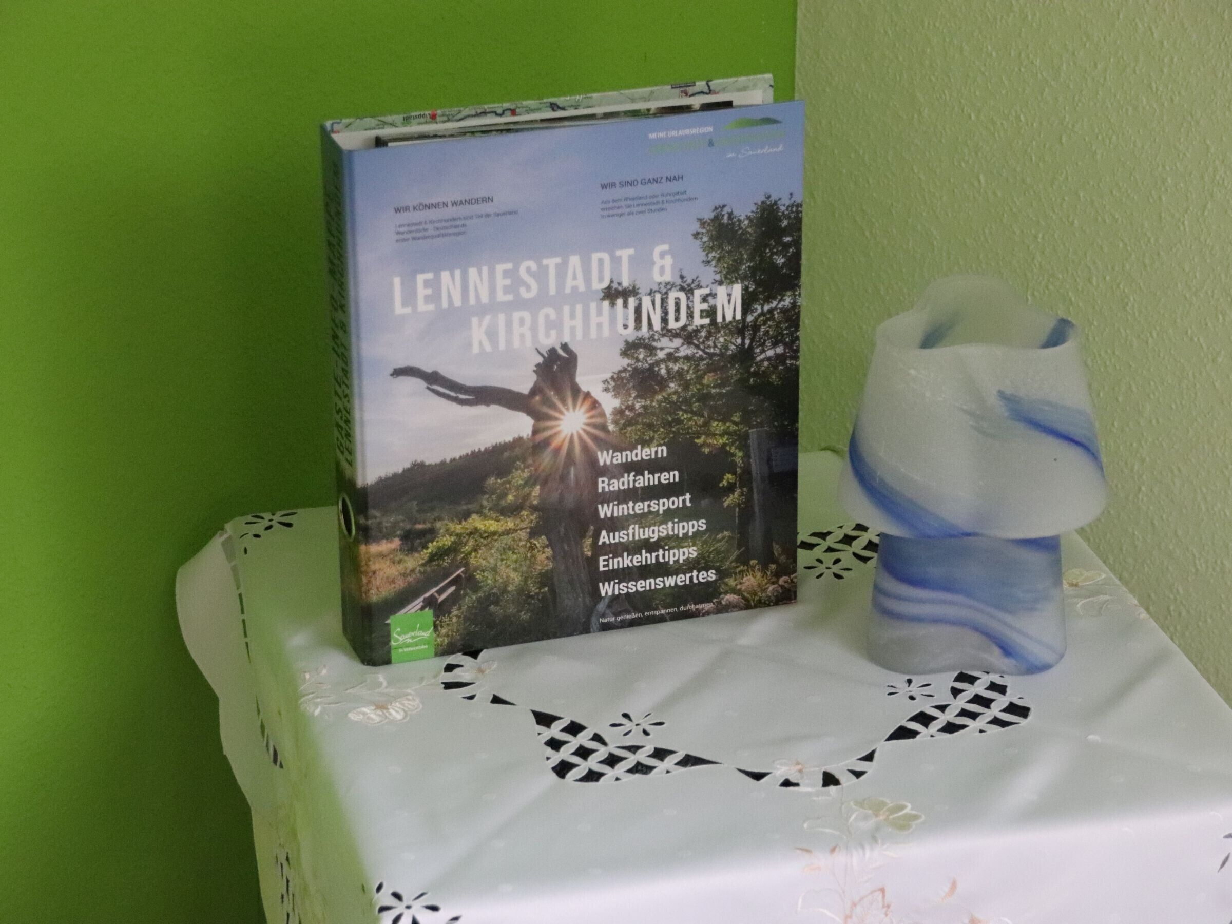 Ein Buch mit dem Titel 'LENNETSTADT & KIRCHHUNDEM' auf einem Tisch mit weißer Tischdecke und einem dekorativen Gegenstand.