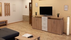A living room with a sofa, a coffee table with remotes, a TV, wooden cabinets, and a stone wall. - Apartment "1 Bartölke" with Private Terrace & Wi-Fi (Bockenem)