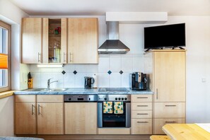 A modern kitchen with wooden cabinets, a stainless steel range, a built-in oven, and a flat-screen TV mounted above the counter. - Apartment "Joachim" with Mountain View, Private Garden & Wi-Fi (Fügen)