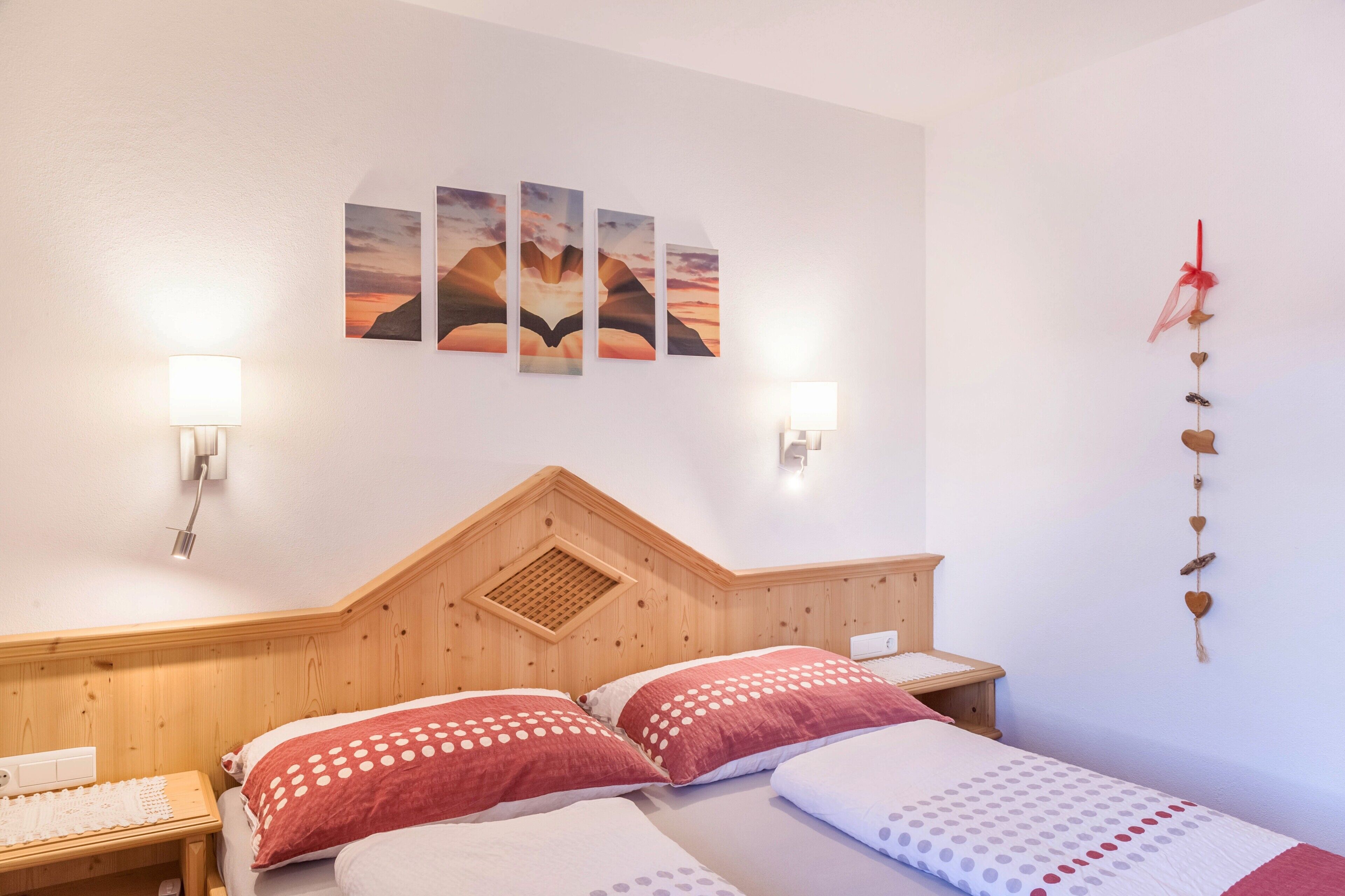A bedroom with a wooden headboard, two beds with polka-dotted bedding, a wall-mounted artwork, and a decorative heart garland.