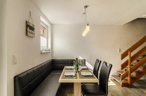A dining area with a wooden table, black chairs, a black cushioned bench, a hanging light fixture, and a staircase.