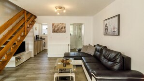 A living room with a wooden staircase, a black leather sofa, a glass coffee table, and a kitchen in the background. - Holiday Apartment 'Nordsee' with Shared Terrace, Shared Garden & Wi-Fi (Hooksiel)