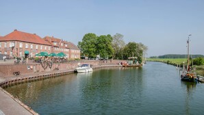 A canal with boats, a brick building, and a green tree. - Holiday Apartment 'Nordsee' with Shared Terrace, Shared Garden & Wi-Fi (Hooksiel)