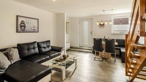 A modern living room with a black leather sofa, a glass coffee table, and a dining area with a wooden table and chairs. - Holiday Apartment 'Nordsee' with Shared Terrace, Shared Garden & Wi-Fi (Hooksiel)