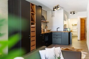 Une cuisine moderne dotée d’appareils électroménagers intégrés, un coin repas avec une table en bois et un salon avec un canapé et un tapis.