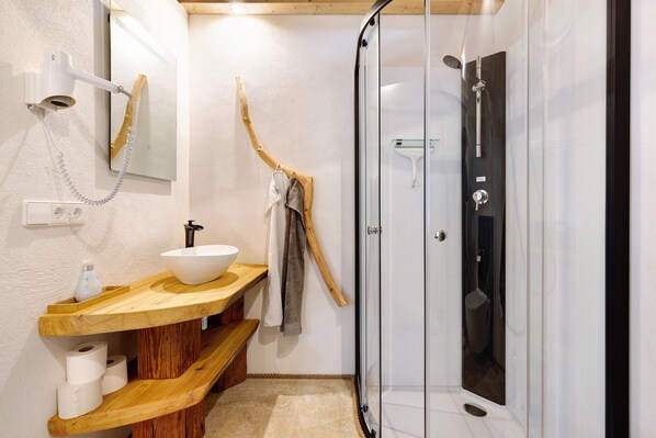 A bathroom with a wooden vanity, a white sink, a glass shower enclosure, and a towel rack.