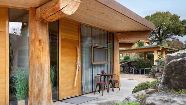 A wooden building with large glass doors, a table with chairs, and a bicycle. - Apartment '-2-die Zwei, Studio 35qm' with Private Terrace, Shared Garden and Wi-Fi (Rosenfeld)