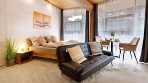 A modern living room with a sofa, a dining table, and a large window. - Apartment '-2-die Zwei, Studio 35qm' with Private Terrace, Shared Garden and Wi-Fi (Rosenfeld)