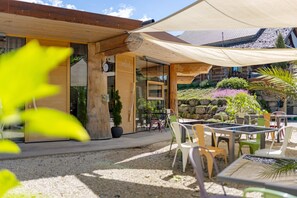 Un bâtiment en bois doté d’un patio couvert, d’un espace extérieur aménagé pour s’asseoir et d’un mur en pierre.