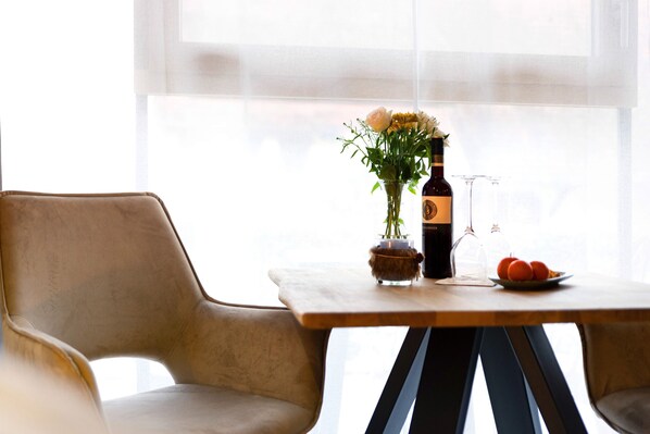Une table avec une bouteille, un vase de fleurs, un verre et une assiette de fruits.