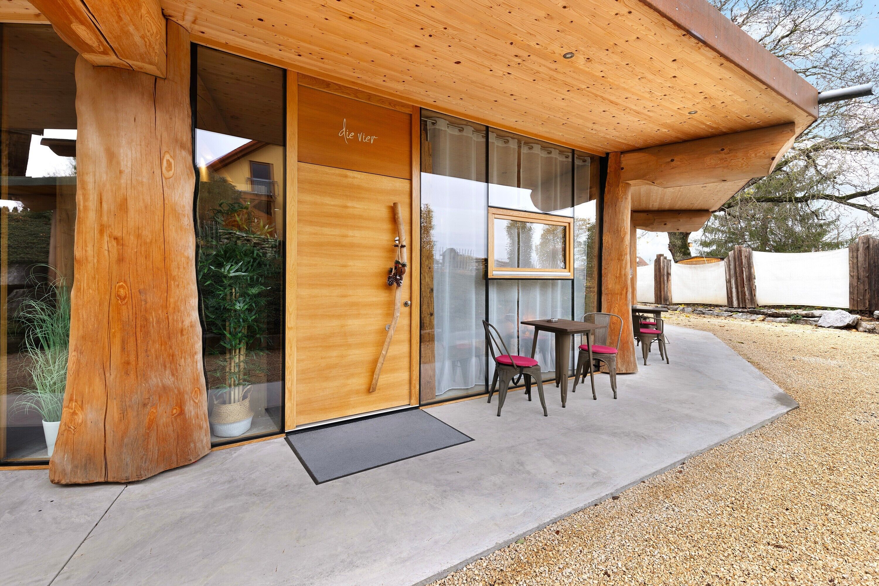 Ein Holzfassade mit einer Schiebetür aus Glas, Sitzgelegenheiten im Freien und einer Holzpergola.