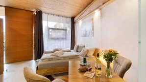 Eine Holzbalkendecke, ein Bett mit Kissen, ein Esstisch mit Blumen in einer Vase und ein Gemälde an der Wand.
