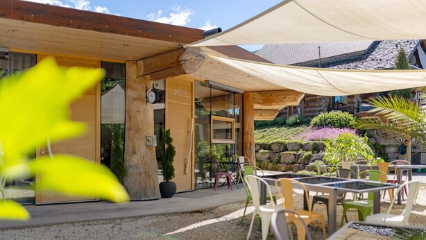 Ein Holzhaus mit überdachter Veranda, Sitzgelegenheiten im Freien und einer Steinwand.