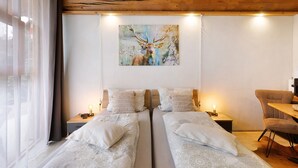 Ein Zimmer mit zwei Betten, einer Holzbalkendecke, einem Hirschbild und einem Sessel.