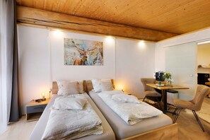 Habitación de hotel con techo de madera, dos camas con ropa blanca, un cuadro de un ciervo, un escritorio con cafetera y una silla.