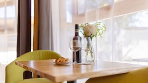 Une table à manger avec une bouteille et des verres, une assiette de nourriture et un vase rempli de fleurs.